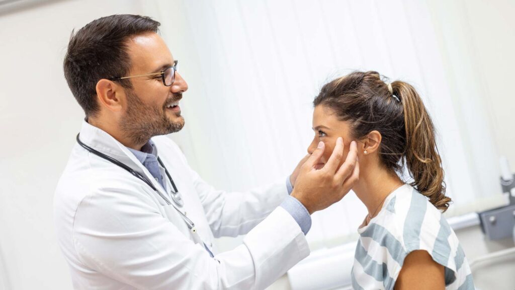 In ear infection treatment in illinois urgent care, a cheerful doctor conducts a thorough facial examination on a young patient, likely part of a routine ear infection check-up.