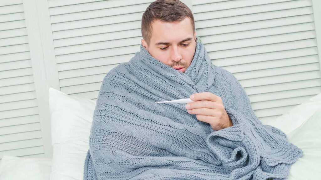 A man wrapped in a blanket checks his temperature, a typical scene at cold treatment in illinois urgent care, where swift action is taken against colds.