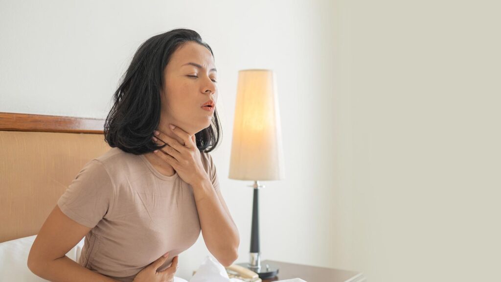 A person appears to be in discomfort holding their throat and stomach, a scene often associated with symptoms treated at mononucleosis treatment in illinois urgent care.