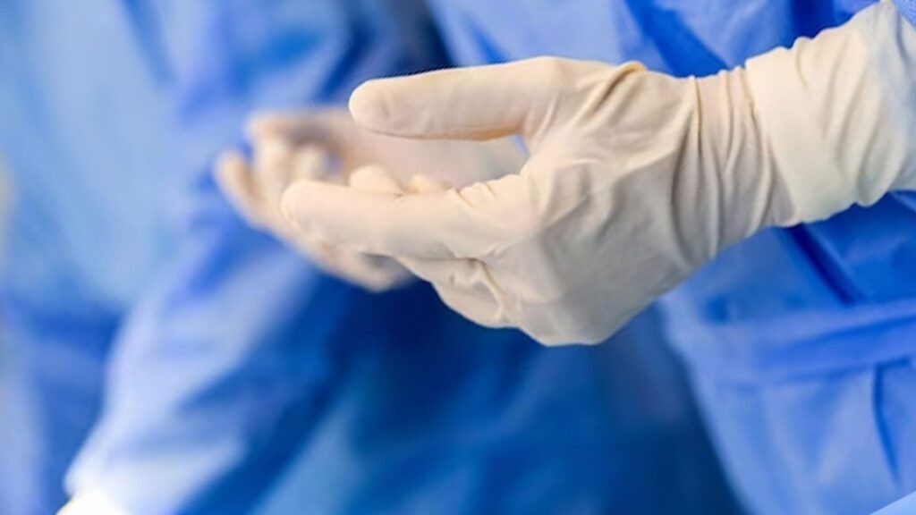 The image captures a close-up of gloved hands against a blue surgical gown background, representing stitch staple removal services in Chicago urgent care clinic.