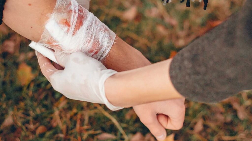 A gloved hand tends to a bandaged wound, demonstrating the compassionate wound cleaning treatment in Chicago urgent care clinic, set against an autumnal backdrop.